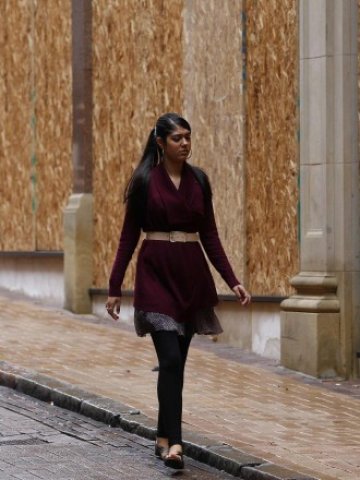 <p>
	Жена минава край закованите с шперплат прозорци на магазини за продажби на дребно в Бирмингам. <em>Снимка: Ройтерс</em></p>
