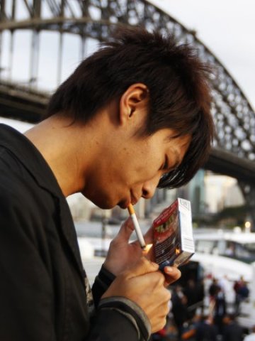 <p>
	<em>Пушач пали цигара на фона Harbour Bridge в Сидни, след като в страната бяха въведени задължителните графични предупреждения върху цигарените опаковки. Снимка: Ройтерс</em></p>
