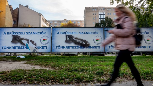 Жена минава покрай унгарски правителствени билбордове, на които пише: &bdquo;Санкциите на Брюксел ни унищожават&ldquo;, изобразявайки санкциите като бомби. Снимка: Janos Kummer/Getty Images
