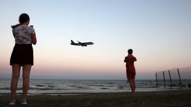 <p>
	Туристи снимат морето, докато самолет се отправя към международното летище в Ларнака. <em>Снимка: Ройтерс</em></p>
