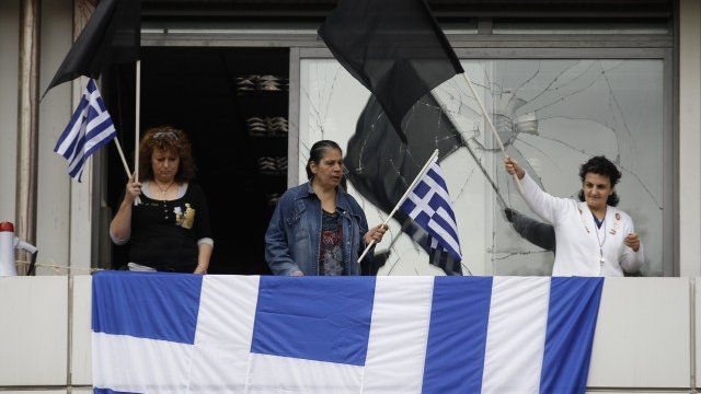 <p>
	Национални и черни знамена се развяват от терасата на гръцкото финансово министерство, чиито прозорци преди това са обстрелвани от протестиращите. <em>Снимка: Ройтерс</em></p>
