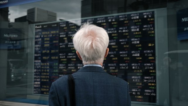 Мъж следи движението на акциите на електронно табло в Токио. Снимка: Soichiro Korimaya/Bloomberg