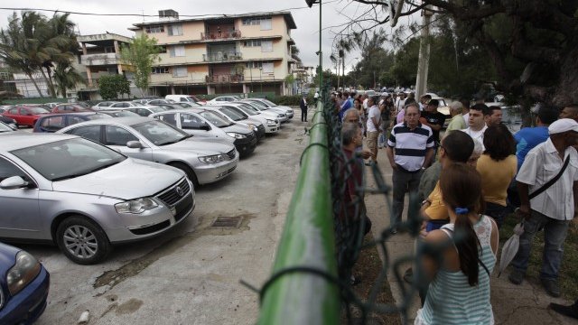 <p>
	Кубинци гледат през оградата автомобили втора употреба, продавани от държавна автокъща. <em>Снимка: Ройтерс</em></p>
