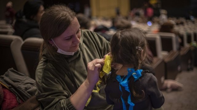 <p>
	Жена връзва панделки в цветовете на украинското национално знаме на косата на момиченце, докато чакат в зала за подпомагане на украински бежанци в Конгресния център в Прага, Чехия. <strong>Снимка: EPA</strong></p>
