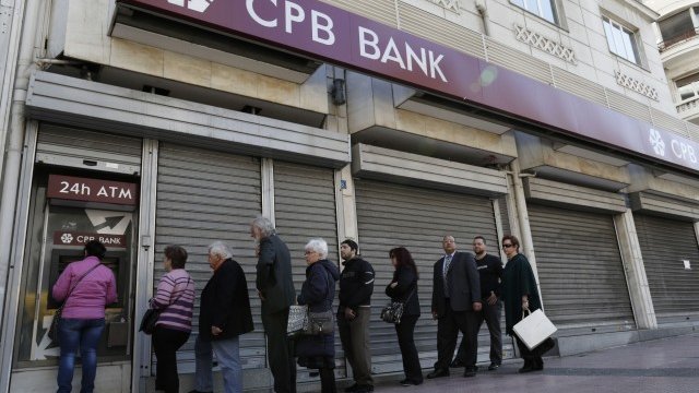 <p>
	Клиенти на нарочената за преструктуриране Cyprus Popular Bank се редят пред банкомат до неин затворен филиал. <em>Снимка: Ройтерс</em></p>
