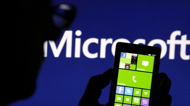 <p>
	Мъж позира със своята Nokia Lumia 820 пред логото на Microsoft.<em>Снимка: Ройтерс</em></p>
