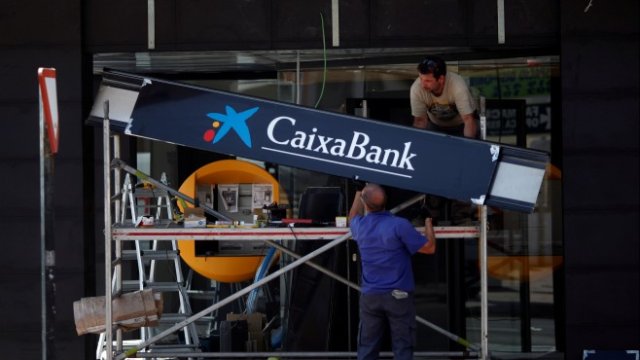 <p>
	Работници окачват логото на банка CaixaBank пред нов офис в Ронда. <em>Снимка: Ройтерс</em></p>
