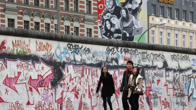 <p>
	Туристи се разхождат покрай най-големия фрагмент от Берлинската стена, запазен в столицата на Германия.<em> Снимка: Архив Ройтерс</em></p>
