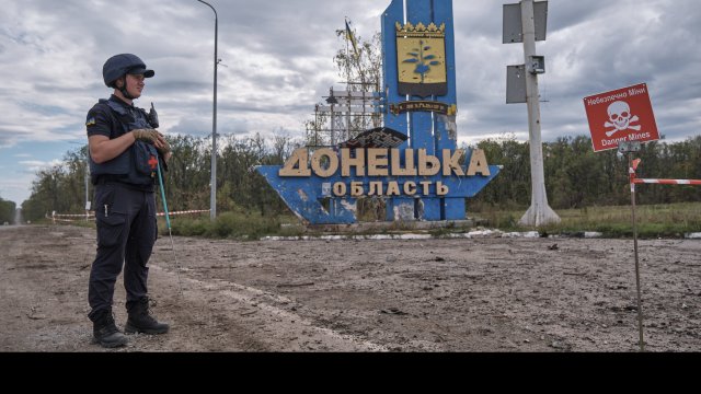 Украински военен стои пред надпис &bdquo;Донецка област&ldquo; на символичната граница между регионите Харков и Донецк и до табела с надпис &quot;Опасни мини&quot;, Украйна, 20 септември 2022 г. Снимка: EPA/YEVGEN HONCHARENKO