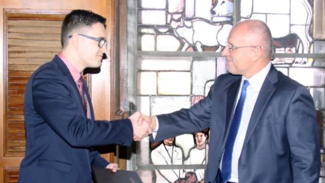 <p>
	Андриан Ямболов, студент в Rheinische Friedrich-Wilhelms-Universitat Bonn, получава удостоверението си за стипендиант на БНБ от гуверньора Димитър Радев.<em> Снимка: БНБ</em></p>
