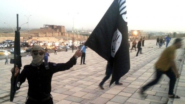 <p>
	Боец на ИДИЛ държи флаг на организацията и оръжие в град Мосул през юни, Снимка: <em>Ройтерс</em></p>
