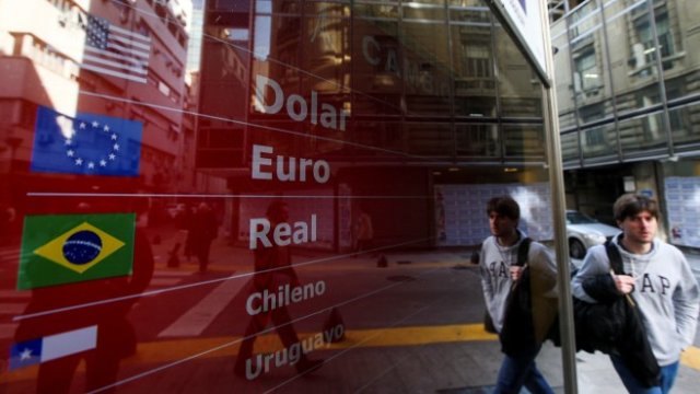 <p>
	Мъж преминава покрай обменно бюро в Буенос Айрес. <em>Снимка: Ройтерс</em></p>
