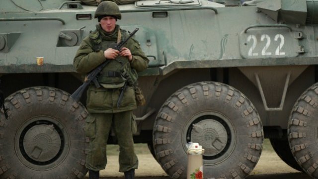 <p>
	Униформен в близост до бронетранспортьор в кримския пристанищен град Феодосия.<em> Снимка: Ройтерс </em></p>
