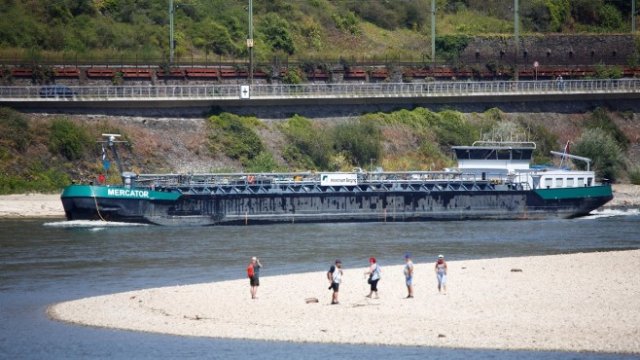 <p>
	Местни се разхождат по пясъчен бряг, обикновено покрит от водите на Рейн, докато холандски танкер се придвижва по пресъхналата река в Обервезел, Германия през лятото на 2018 г. <em>Снимка: Архив Ройтерс</em></p>
