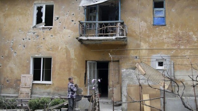 <p>
	Мъж разчиства отломки около една от полуразрушените заради боевете жилищни сгради в Донецк. <em>Снимка: архив, Ройтерс</em></p>
