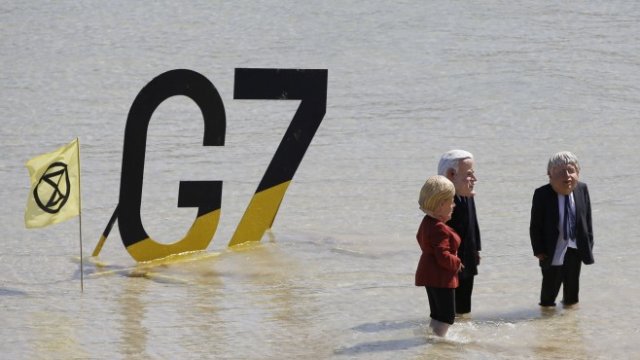 <p>
	Протестиращи от Extinction Rebellion пред знака на Г-7 с маски, изобразяващи Ангела Меркел (вляво), американския президент Джо Байдън и Борис Джонсън (вдясно), в последния ден от срещата на върха на Г-7в Сейнт Айвс, Великобритания. <em>Снимка: Hollie Adams/Bloomberg</em></p>
