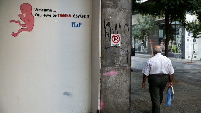 <p>
	Минувач в Атина се разхожда покрай графит на уличния артист Flip, изобразяващ неродено дете с думите &bdquo;Добре дошъл... ти дължиш на Тройката 36 730 евро&quot;. <em>Снимка: Ройтерс</em></p>
