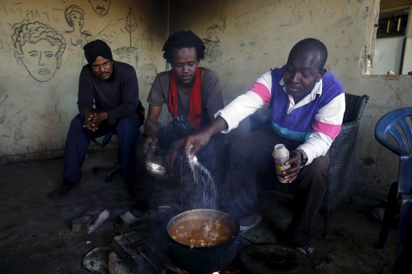 
	Трима суданци пред импровизирана кухня в изоставена фабрика.
