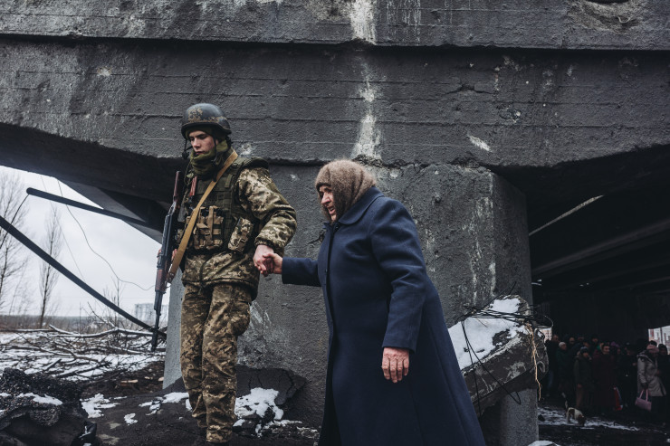 Украински военен помага на жена да премине през разрушен мост в Изюм. Снимка: Diego Herrera Carcedo/Anadolu Agency via Getty Images)