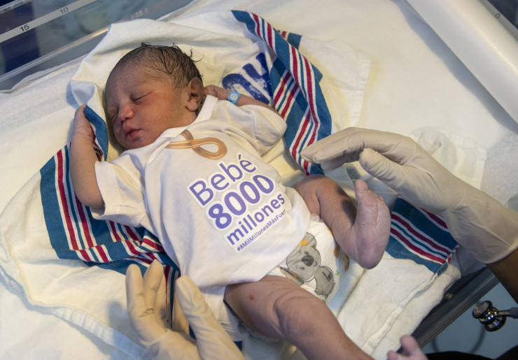 Медицинска сестра слага тениска с надпис "8-милиардно бебе" на новородения Дамян в родилния дом "Алтаграсия" в Санто Доминго, Доминиканска република. Дамян, първото регистрирано бебе, което се роди в страната на 15 ноември 2022 г., е символично избран да представлява приноса на страната към броя на населението на света от 8 млрд. души. Снимка: EPA/ORLANDO BARRIA  