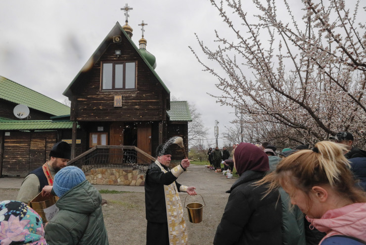 Украински свещеник благославя вярващите с кошници с боядисани яйца и куличи - традиционен великденски сладкиш, по време на православна великденска меса пред малка църква в жилищен квартал в Киев, Украйна. Снимка: EPA/SERGEY DOLZHENKO