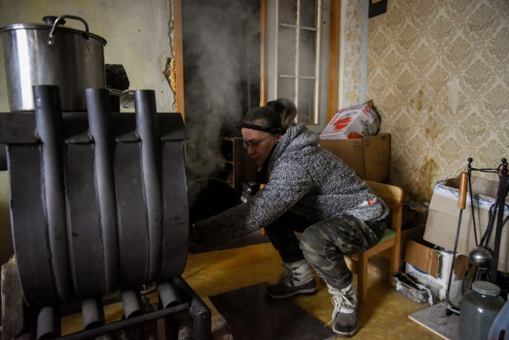 Тетяна зарежда печка с дърва в апартамента си в разрушен жилищен блок в Горенка, близо до Киев. Тетяна и съпругът ѝ Ихор се завръщат в апартамента си през април, след като жилищният блок е повреден от руски обстрел по време на боевете в Киевска област през март миналата година. Снимка: EPA/OLEG PETRASYUK
