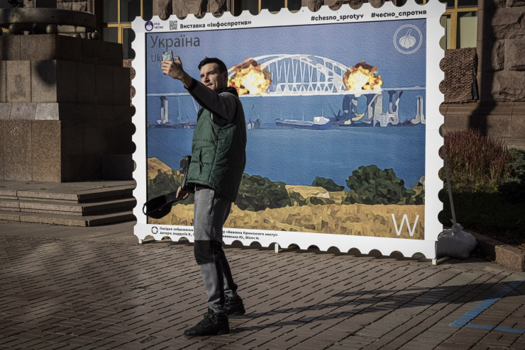 Хора позират за снимки пред кадър на пощенска марка, на която е изобразен горящият Кримски мост на 8 октомври 2022 г. в центъра на Киев, Украйна. Снимка: Getty Images News
