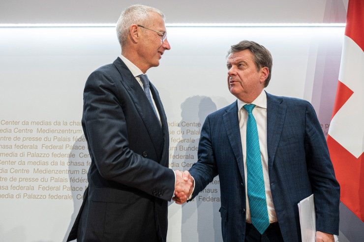 Аксел Леман, председател на Credit Suisse Group AG, вляво, и Колм Келехер, председател на UBS Group AG, си стискат ръцете след пресконференция в Берн, в неделя. Снимка: Pascal Mora/Bloomberg